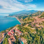 View from flying drone. Sunny morning view of Taormina town and Etna volcano on background. Nice spring seascape of Mediterranean sea. Splendid view of Sicily, Itale, Europe.
